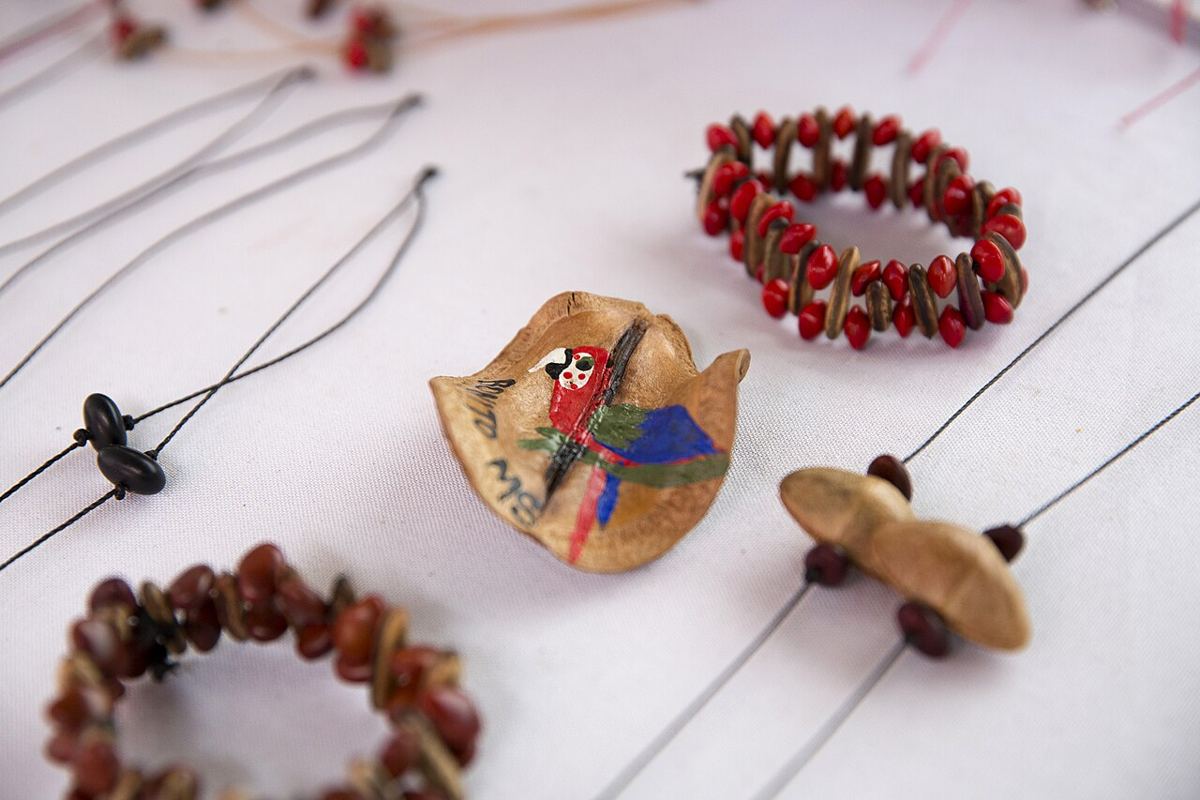 Pulseiras e colares feitos com sementes vermelhas e marrons, e um pingente de casca pintado com uma arara.