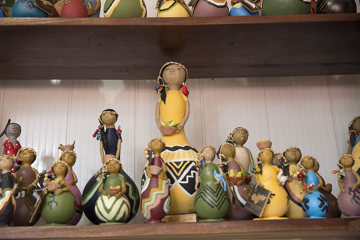 Bonecas feitas de cabaça pintada com padrões coloridos, em uma prateleira de madeira.