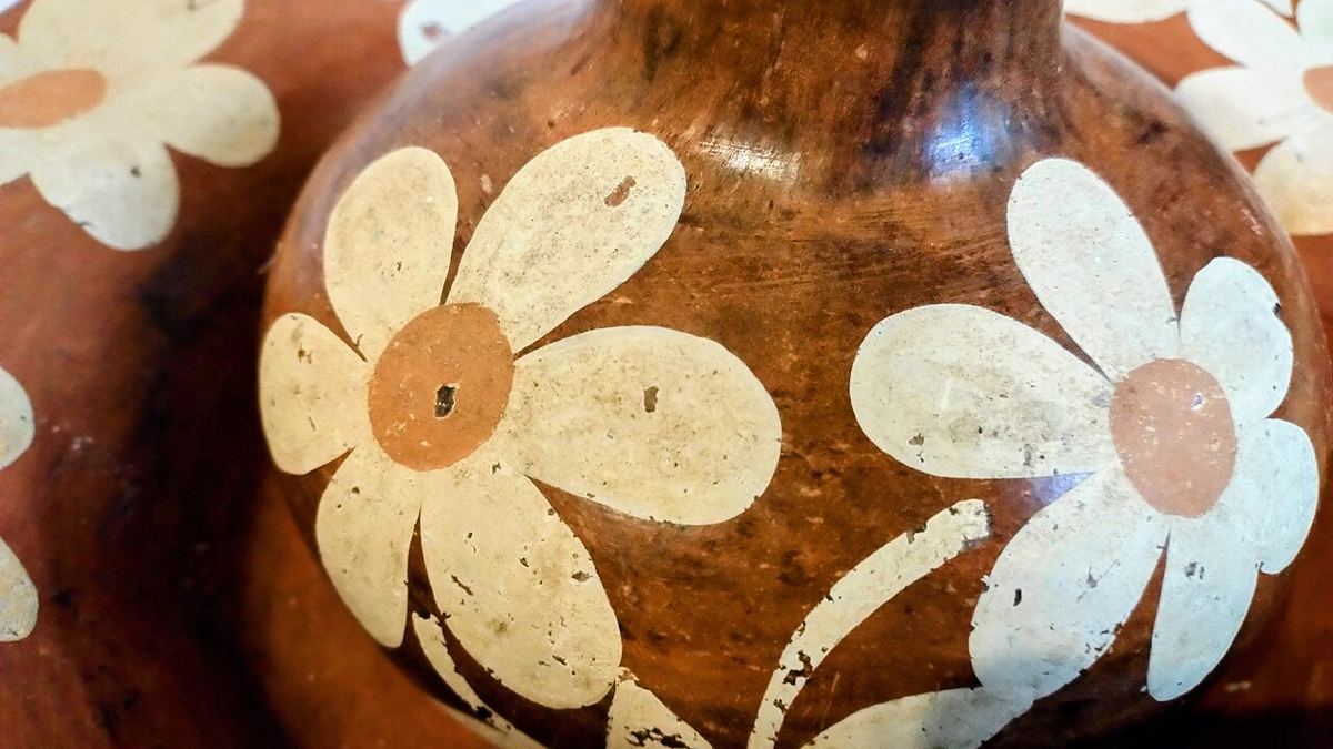 Detalhe de uma jarra de cerâmica marrom pintada com grandes flores brancas.